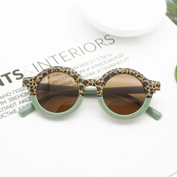 Un par de gafas de sol con la montura mitad verde y la otra mitad con un motivo animal colocadas en la página de una revista