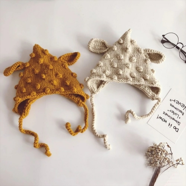 Sobre un soporte blanco, hay dos sombreros colocados uno al lado del otro, uno marrón a la izquierda y otro beige a la derecha. También hay un trozo de papel con algo escrito y unas gafas