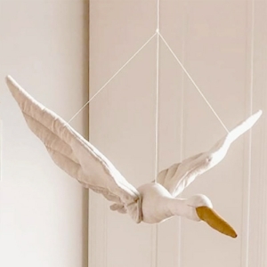 Muñeca en forma de cisne blanco con pico beige que cuelga de tres cuerdas delante de una pared blanca