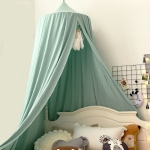 Cuna de bebé verde colgada sobre una cama blanca con cojines blancos, beige y grises delante de una pared blanca