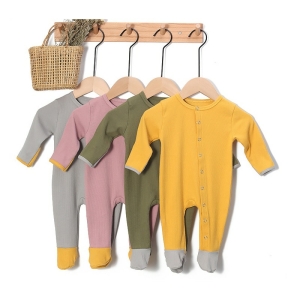 Pelele de bebé acanalado en algodón amarillo, verde, rosa y gris colgado de perchas en un perchero de pared beige con una cesta de mimbre