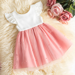 Vestido de tul blanco y rosa con mangas cortas con volantes para niña tumbada sobre una alfombra de pelo largo junto a rosas del mismo color