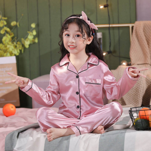 Chica joven sentada con las piernas cruzadas en pijama de satén rosa