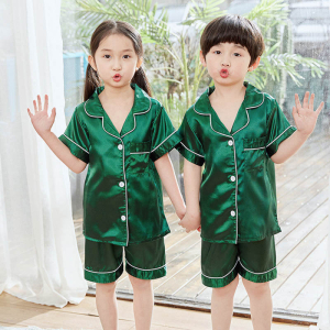 Niña y niño de pie, con una mano levantada, vistiendo un pijama de satén verde