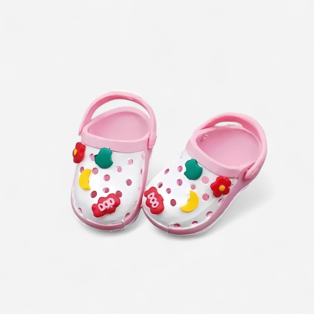 Mini zuecos estilo Crocs de color rosa y blanco, con pequeños charms coloridos en la parte superior, sobre fondo neutro